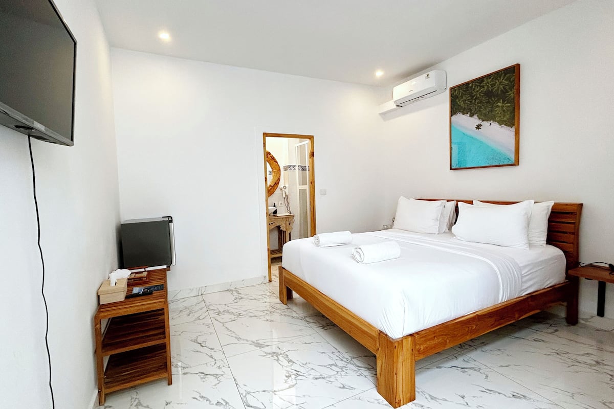 A hotel room with a bed, a TV, a painting, and an air conditioning unit.