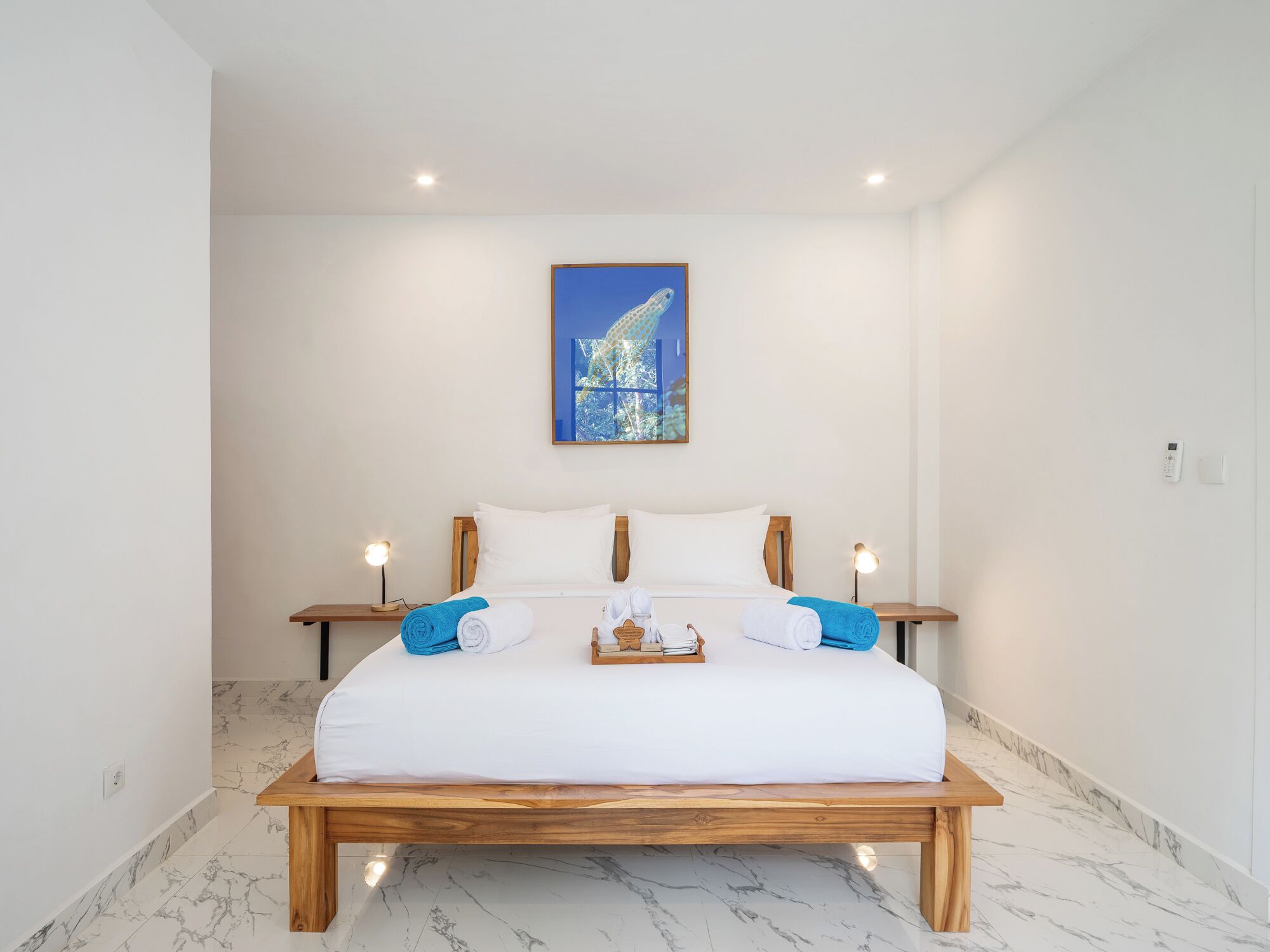Una habitación de hotel con una cama grande, dos mesitas de noche, una lámpara de noche, un cuadro en la pared y suelo de mármol.