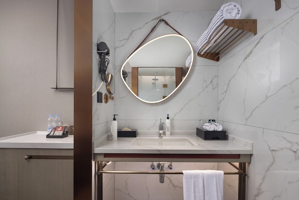 A modern bathroom with a marble sink, a large mirror with a light, and a towel rack.