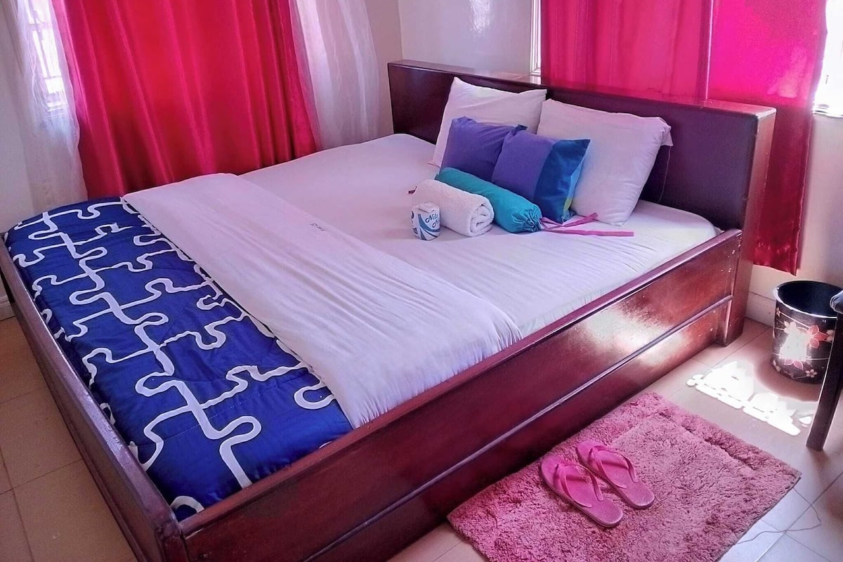 A neatly made bed with a patterned bedspread, pillows, and a rolled towel.
