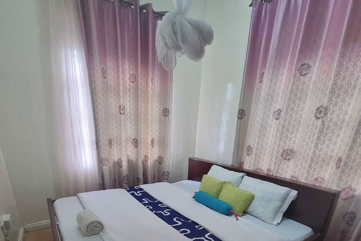 A neatly made bed with a blue and white patterned bedspread, pillows, and a rolled towel.