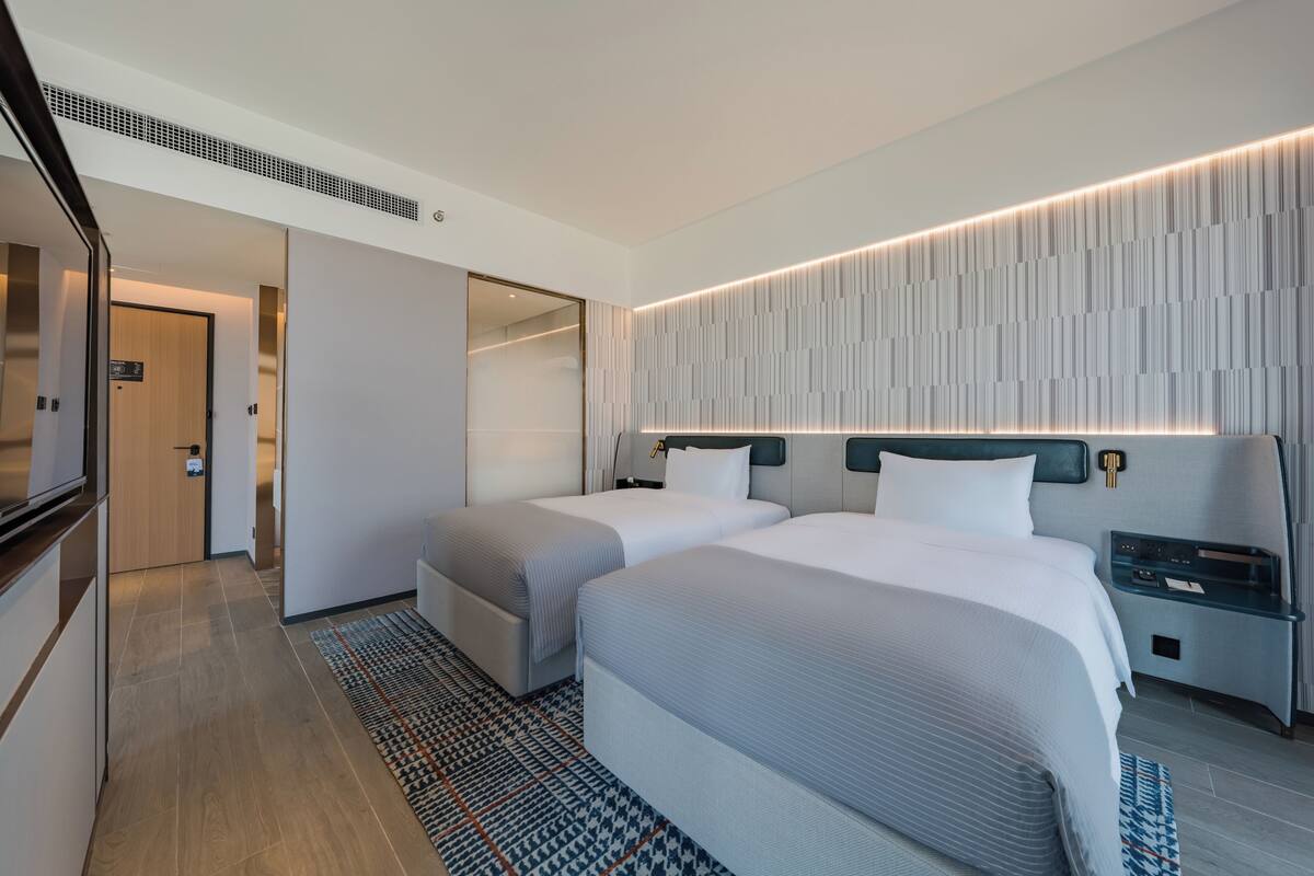 A hotel room with two beds, a modern headboard, a nightstand, and a patterned rug.