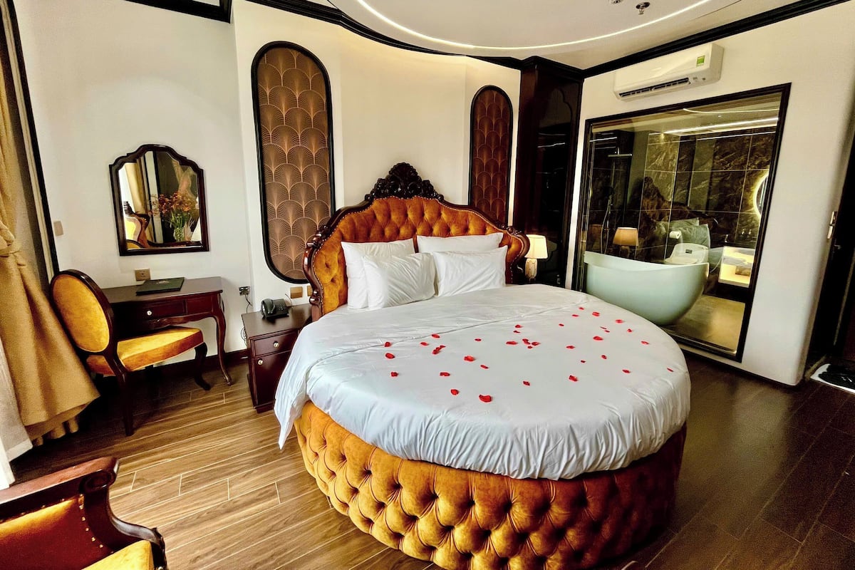 A hotel room with a large bed, a desk, a chair, a mirror, and a bathroom visible through an open door.