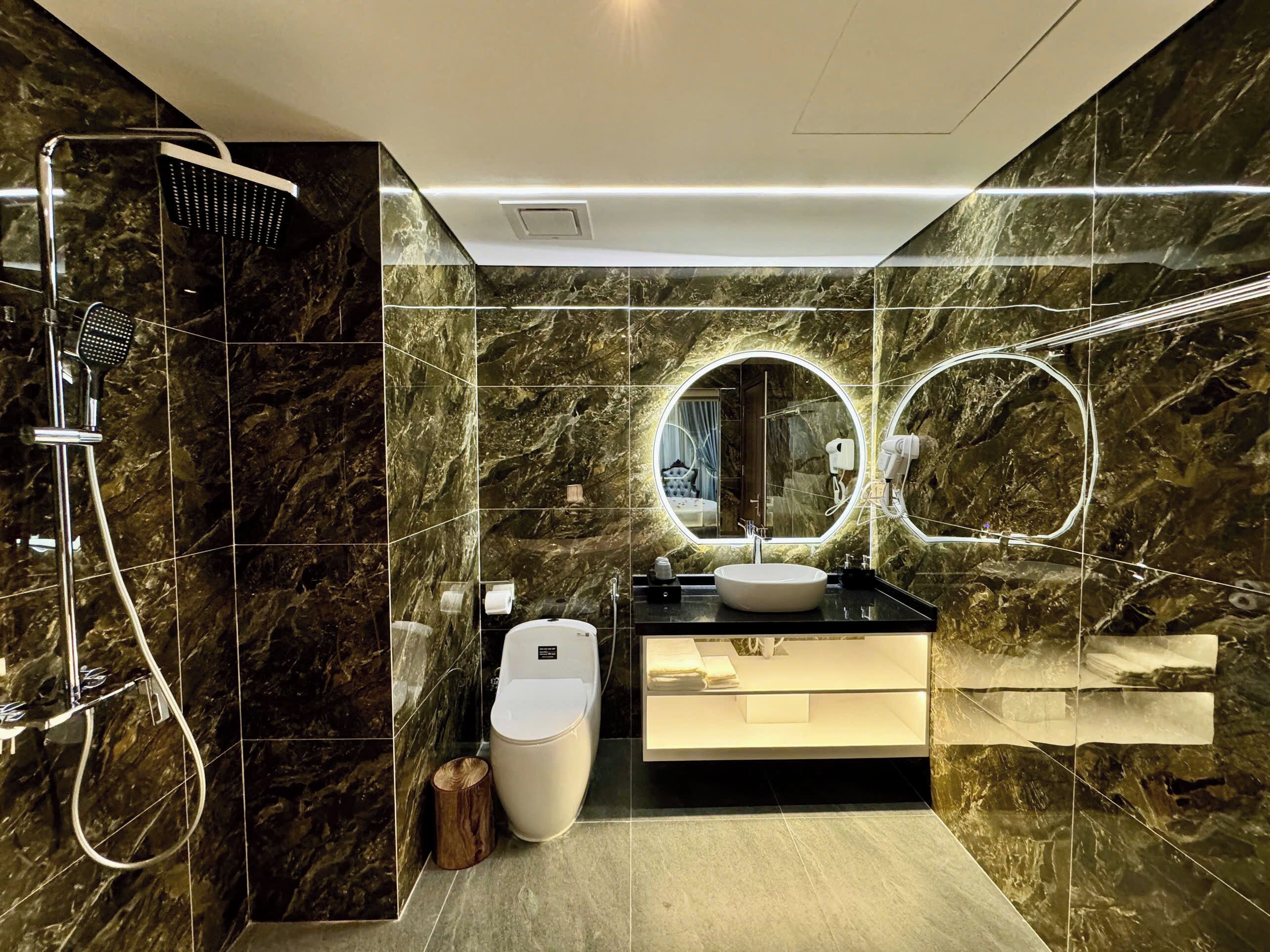 A modern bathroom with a marble wall, a round mirror, a white sink, and a shower with a handheld showerhead.