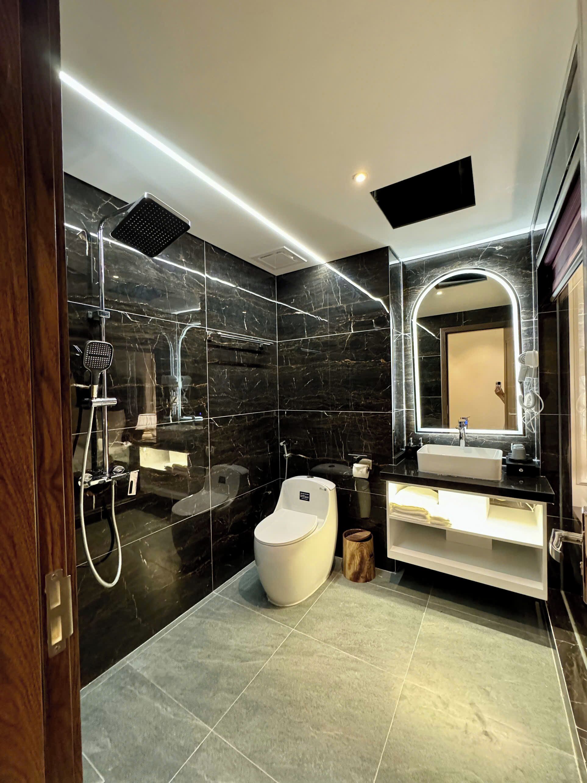A modern bathroom with a black marble wall, a white toilet, a bathtub, and a vanity with a mirror.