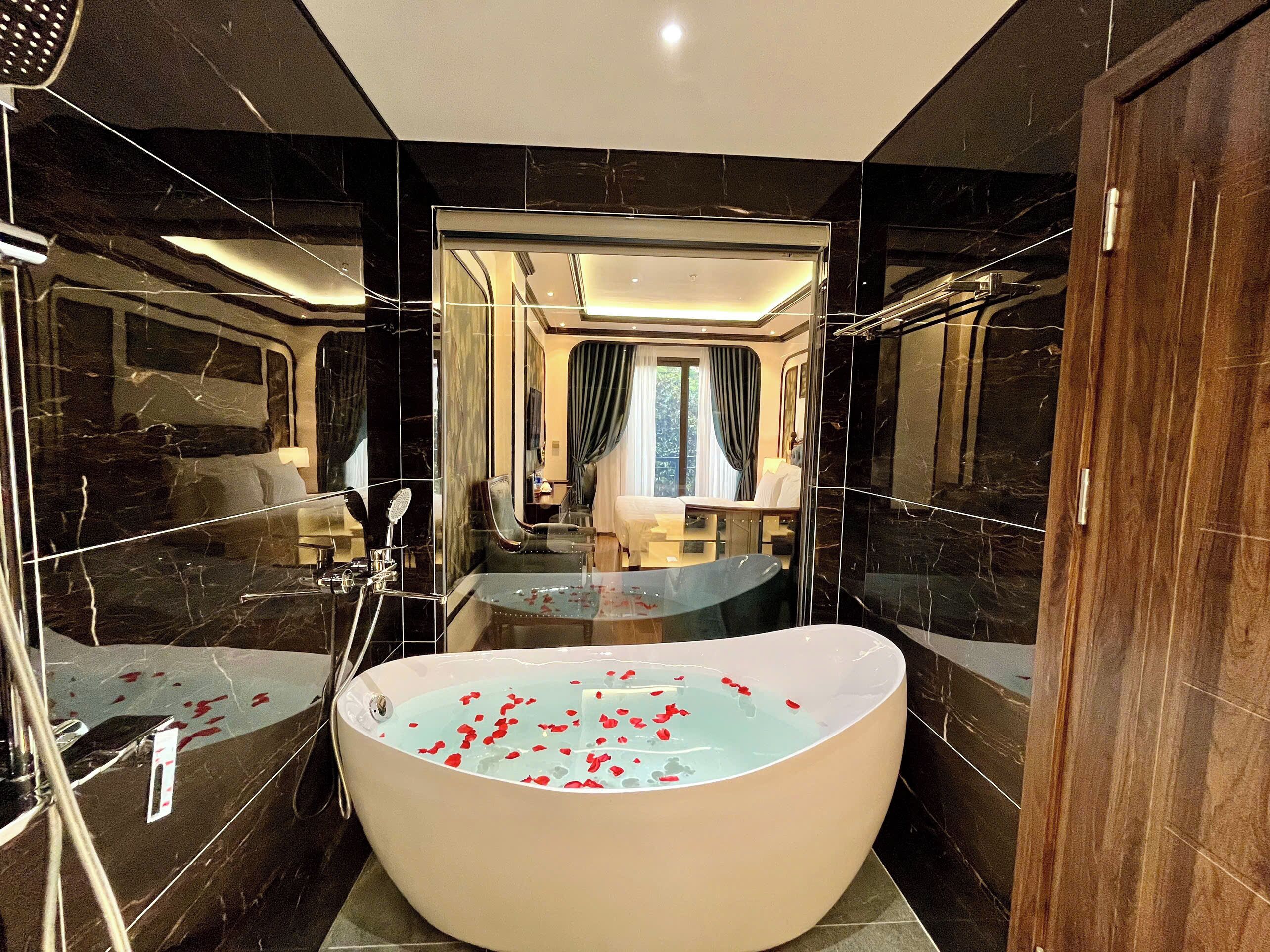 Un baño moderno con una bañera independiente grande llena de pétalos de rosa, una zona de ducha con mampara de cristal y un tocador con espejo.