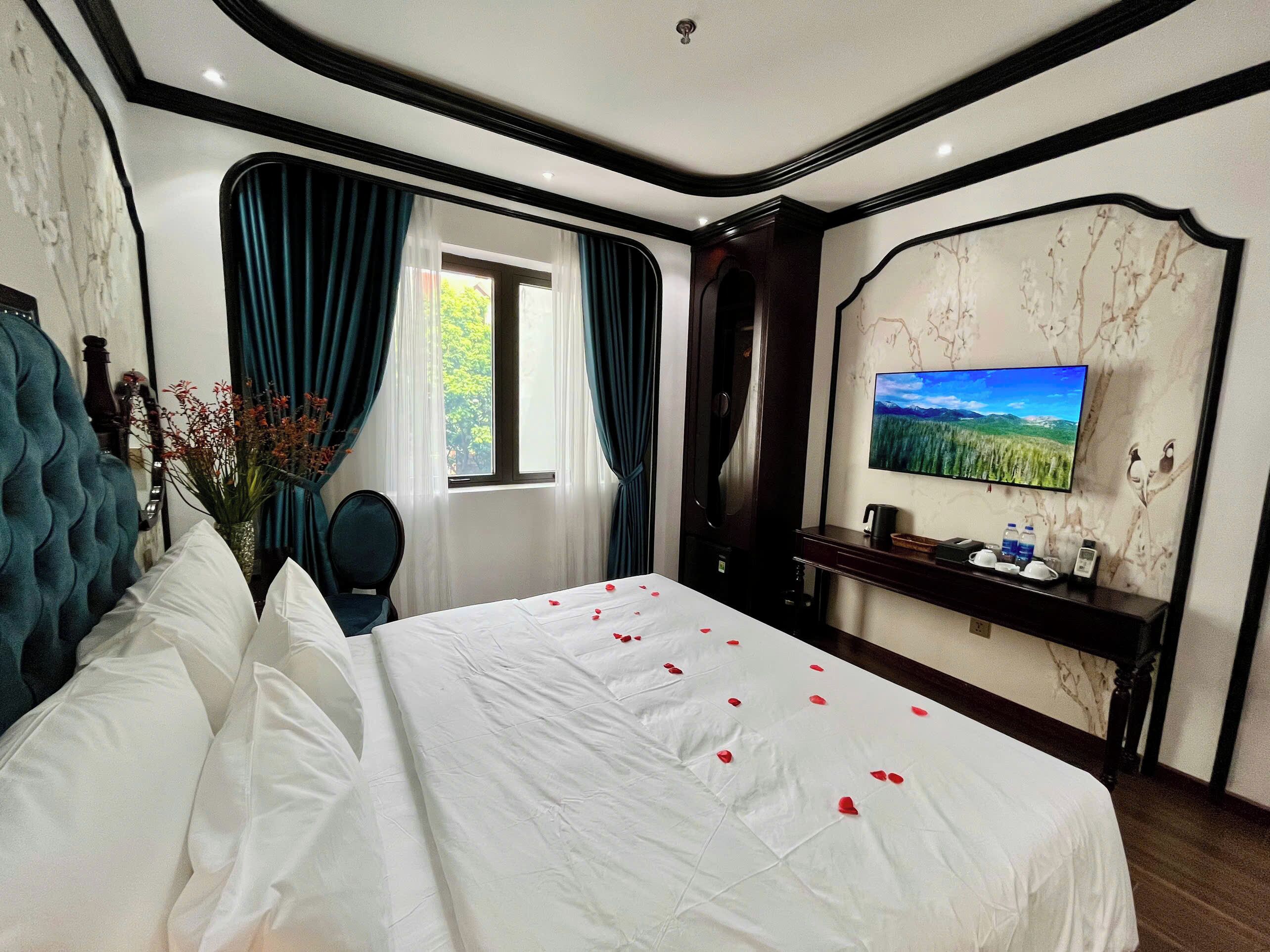 A hotel room with a bed, a TV, a desk, and a window with curtains.