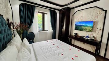 A hotel room with a bed, a TV, a desk, and a window with curtains.