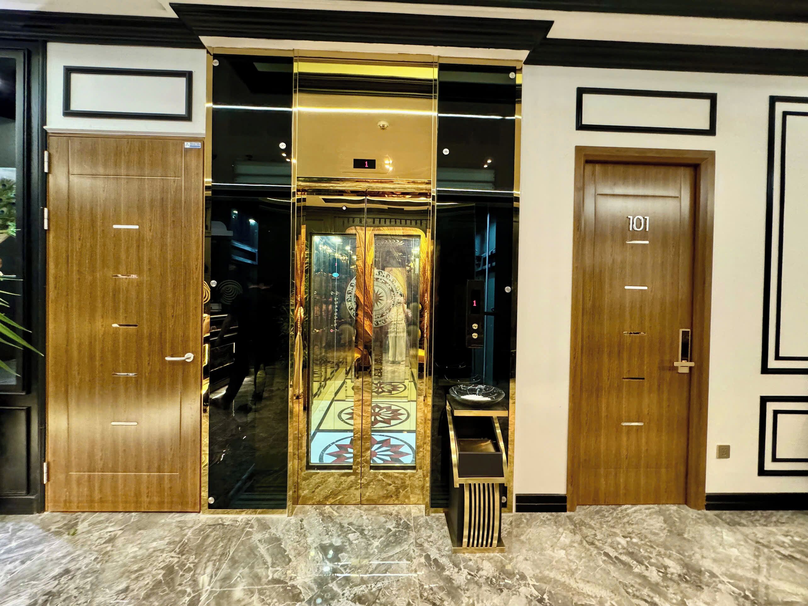 L’entrée d’un hôtel, avec une porte en verre, un sol en marbre et deux portes en bois portant l’inscription « 101 ».