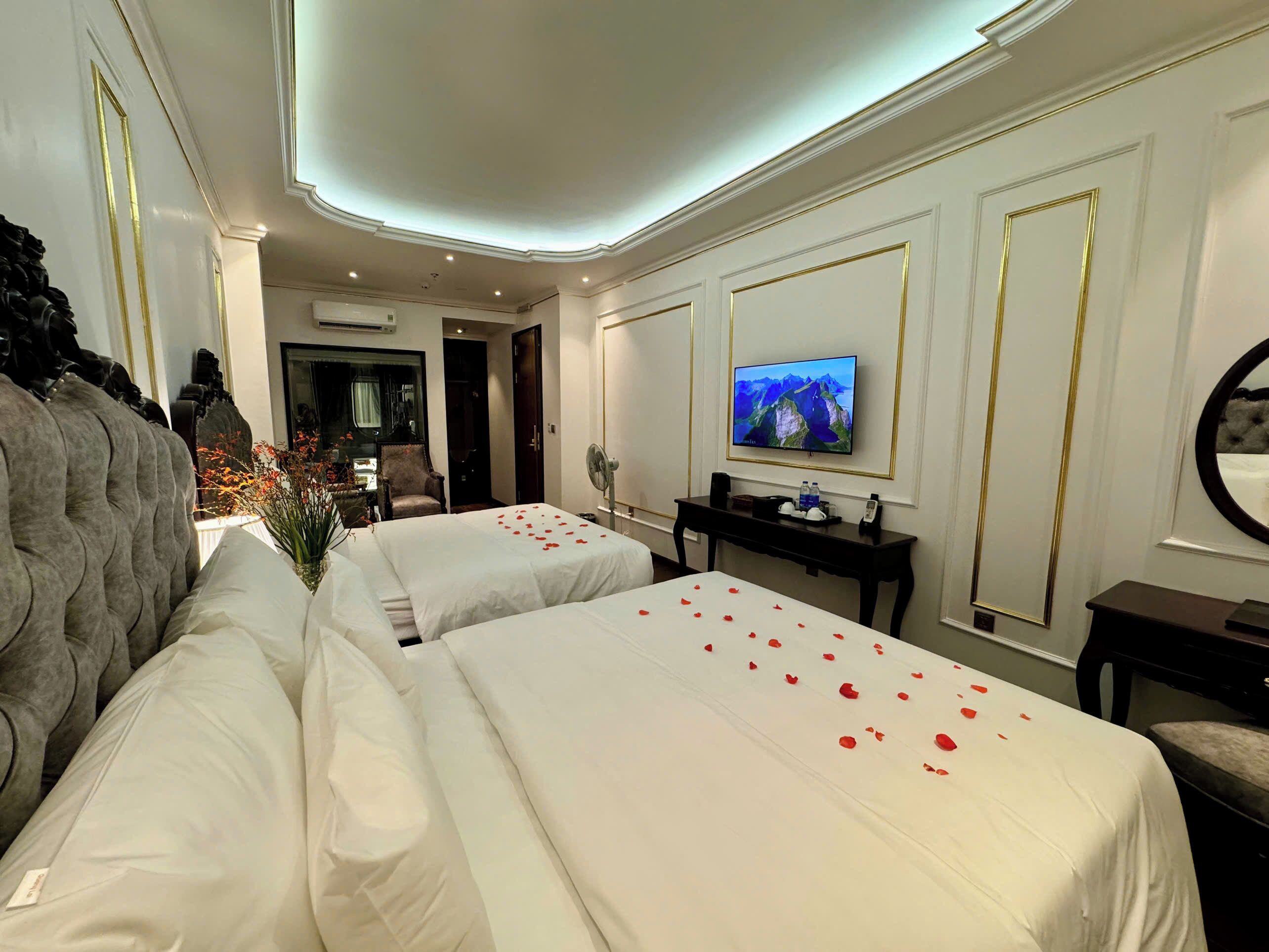 Quarto de hotel com duas camas, televisão, escrivaninha e espelho.