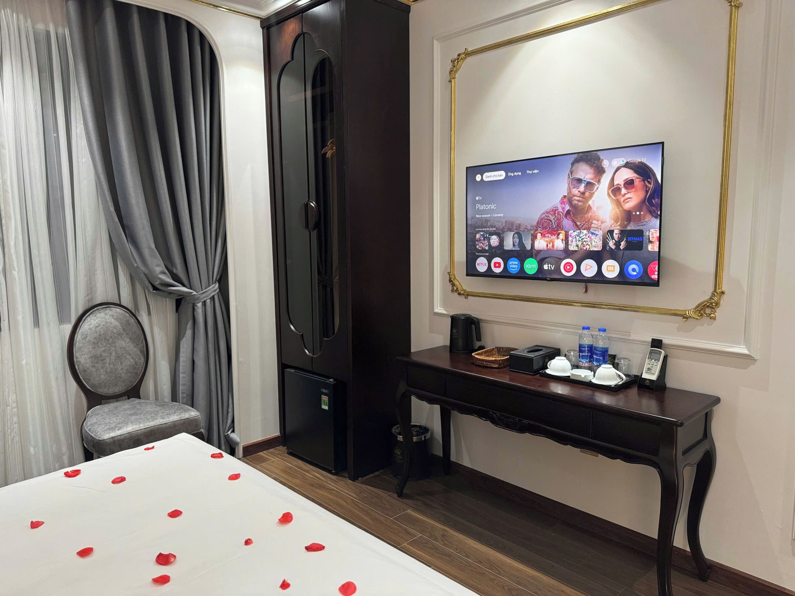 A hotel room with a bed, a television mounted on the wall, a desk with a kettle, and a wardrobe.