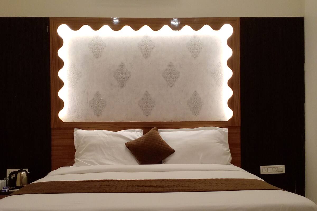 A hotel room with a large bed, a wooden headboard with a lighted panel, and an air conditioning unit above the bed.