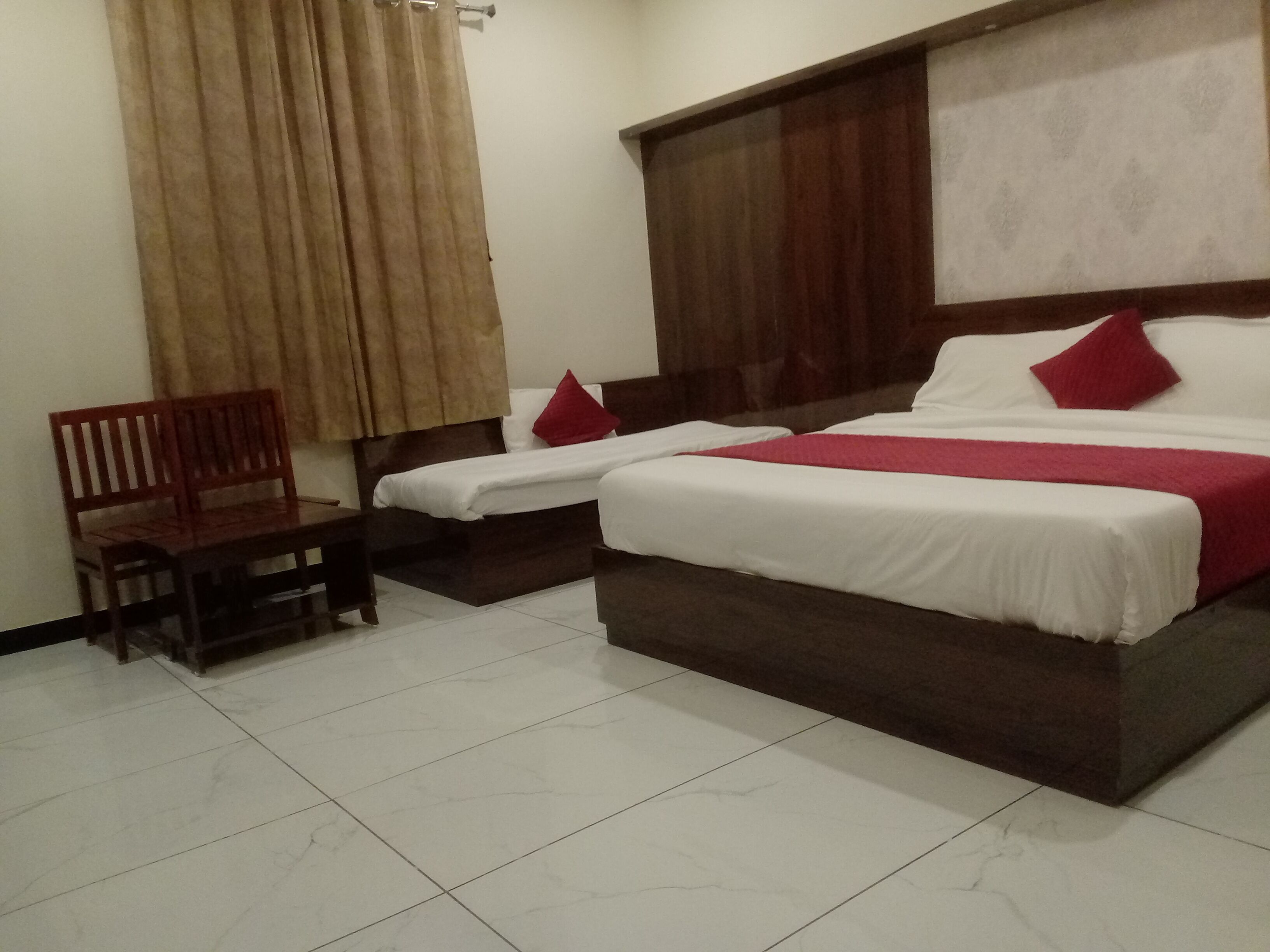 A hotel room with two beds, a wooden chair, and a large window with curtains.
