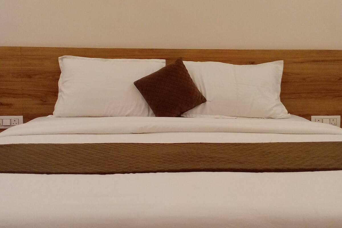 A bed with white bedding and a brown pillow, a wooden headboard, and a white wall.