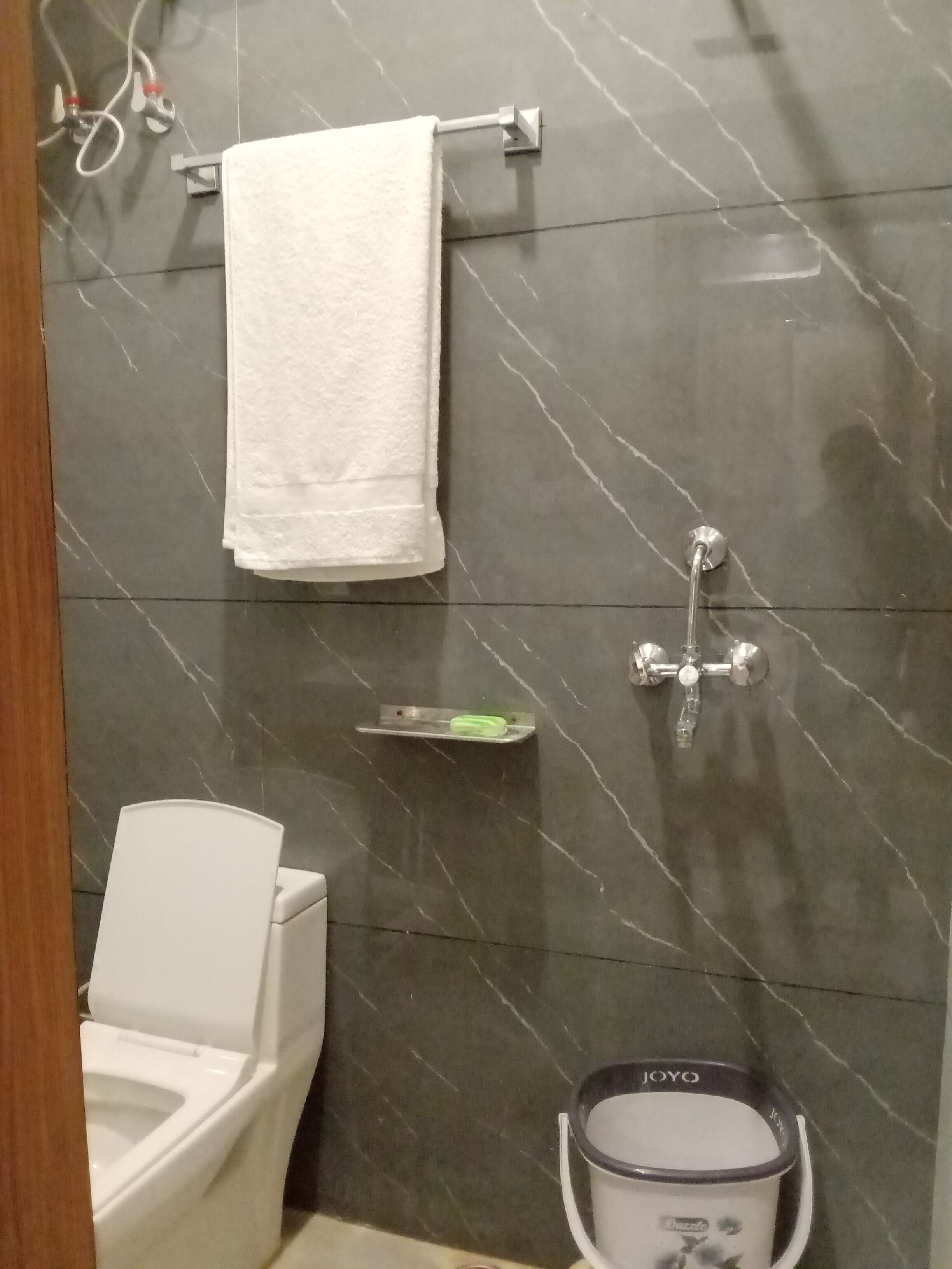 A bathroom with a toilet, a towel rack, a showerhead, and a soap dish.