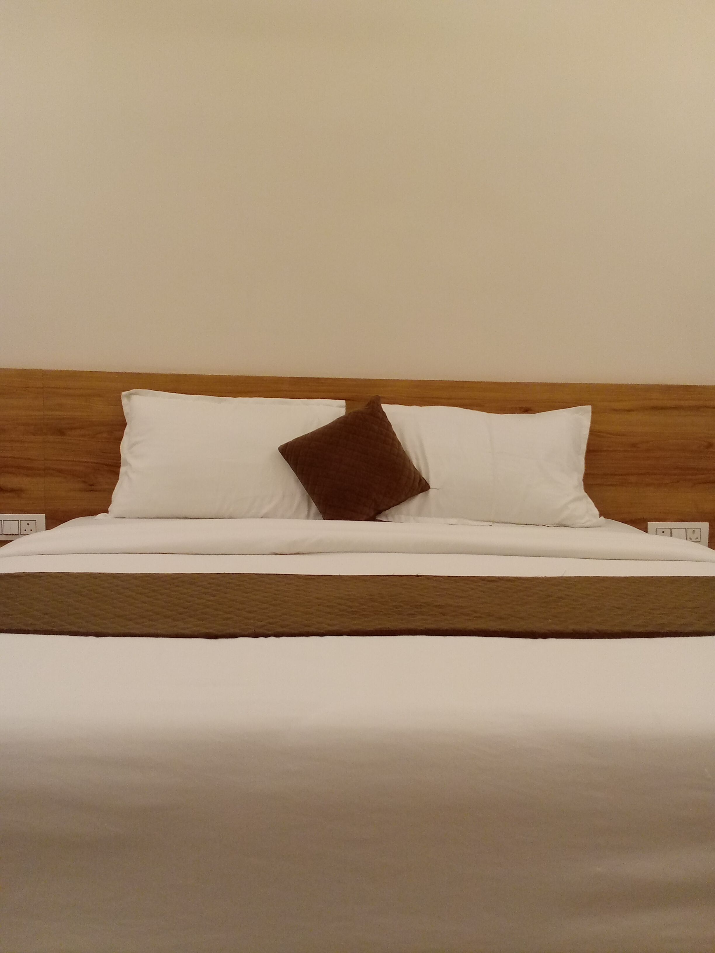 Un lit avec une literie blanche et un oreiller marron, une tête de lit en bois et un mur sobre.