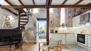 A spacious living area with a wooden floor, a large flat-screen TV, a comfortable chair, and a staircase leading to an outdoor area. - Charming Stone House near Beach Retreat (Vilaür)
