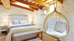 A bedroom with a wooden ceiling, a hanging chair, a bed with pillows, a bedside table, and a wall-mounted air conditioner. - Charming Stone House near Beach Retreat (Vilaür)