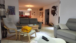 A living room with a grey sofa, a wooden chair, a small white table, and a remote control on the table.