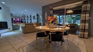 A modern living room with a dining area, a television, and a large window with curtains.