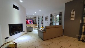 A living room with a flat-screen TV, a beige sofa, and a dining area with a table and chairs.