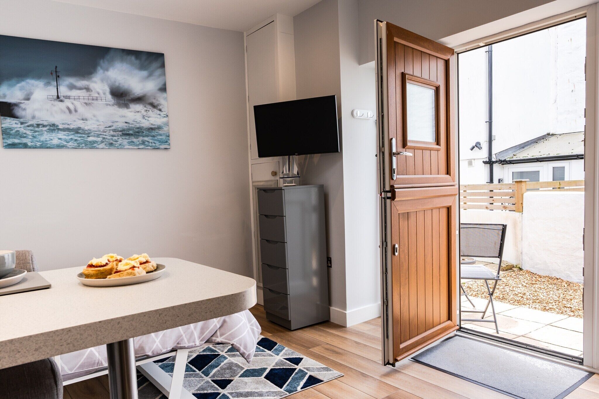 A room with a dining table, a television, a cabinet, and a door leading to an outdoor area.