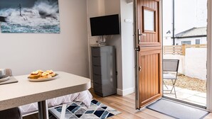 A room with a dining table, a television, a cabinet, and a door leading to an outdoor area.