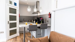 A modern kitchen with a white countertop, two bar stools, and a coffee machine.
