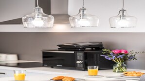 A modern kitchen with a microwave, toaster, and a glass of orange juice on the counter.