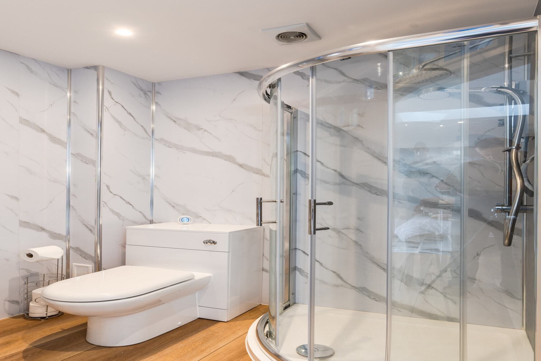 Un baño moderno con ducha envuelta en vidrio, inodoro blanco y paredes con diseño de mármol.