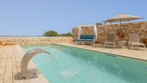 A pool area with a stone wall, lounge chairs, and a canopy umbrella. - Villa Regina on the Sea (Carovigno)