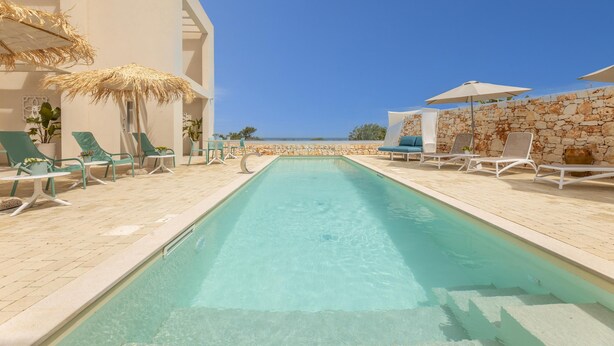 A pool area with lounge chairs and umbrellas, a stone wall, and a clear view of the sea. - Villa Regina on the Sea (Carovigno)