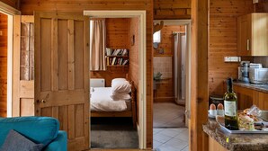 A cozy cabin interior with a wooden door leading to a bedroom, a kitchen area with a dining table, and a bookshelf. - Cottage by Mawddach Trail with Stunning Views (Dolgellau)