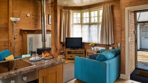 A cozy cabin interior with a kitchen area, a television, and a seating area with a blue sofa. - Cottage by Mawddach Trail with Stunning Views (Dolgellau)
