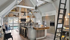 A spacious kitchen with a central island, wooden flooring, and a lofted dining area with clear chairs. - Apartment in Dartmouth near Waterfront (Dartmouth)