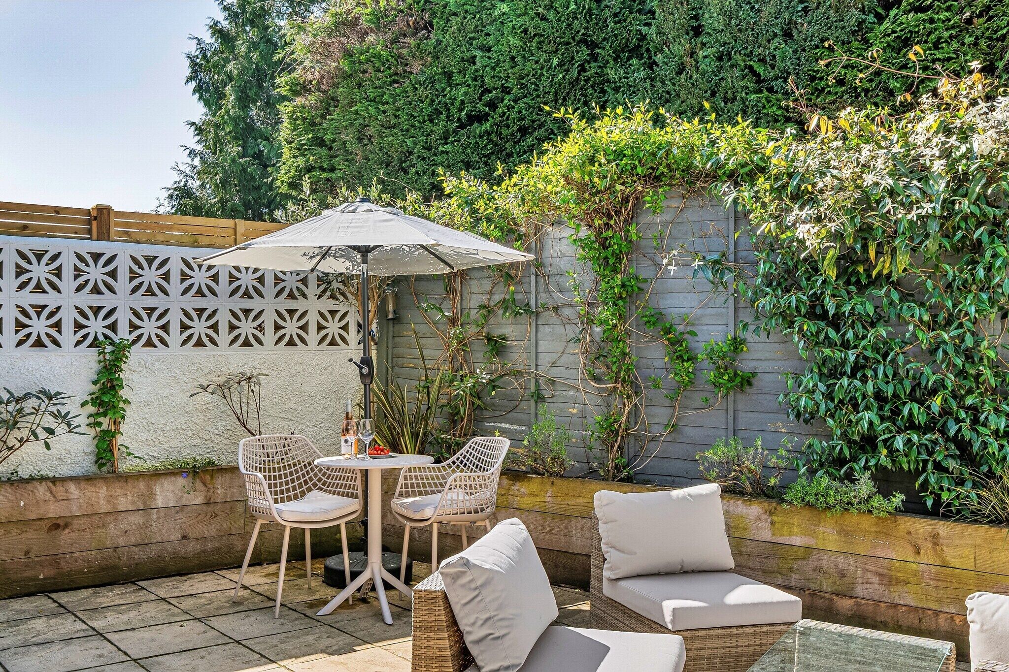 Une terrasse extérieure avec des meubles en osier, une table à plateau en verre et un parasol.