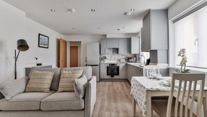 Un salon moderne avec un canapé gris, une table à manger recouverte d’une nappe blanche et une cuisine en arrière-plan.