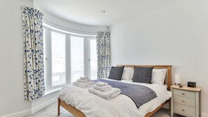 Et soveværelse med seng, et natbord og et vindue med gardiner.