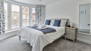 A bedroom with a bed, nightstand, and a large window with curtains. - Apartment in Filey near the Beach (Filey)