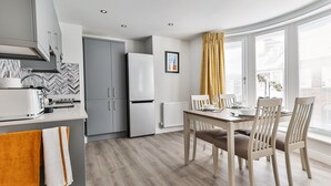 A modern kitchen with grey cabinets, a white refrigerator, and a dining area with a wooden table and chairs. - Apartment in Filey near the Beach (Filey)