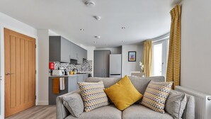A modern living room with a grey sofa, two patterned cushions, and a window with curtains. - Apartment in Filey near the Beach (Filey)