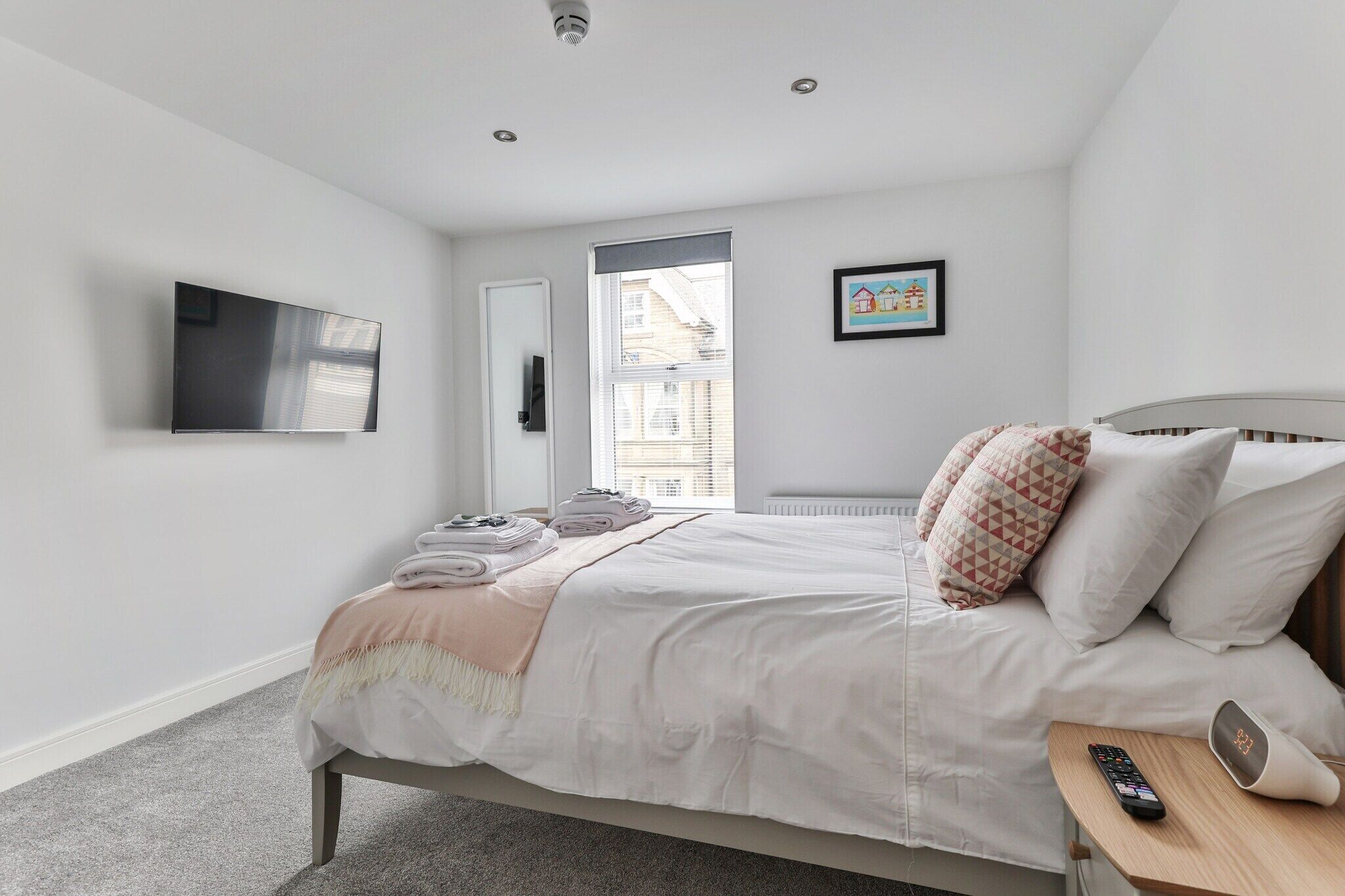 A bedroom with a bed, a TV mounted on the wall, a window with blinds, and a framed picture on the wall.