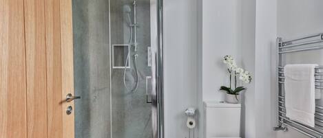 A modern bathroom with a glass-enclosed shower, a white toilet, a sink, and a towel rack.