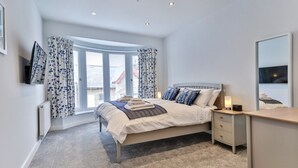 A bedroom with a bed, bedside table, lamp, and a large window with curtains.