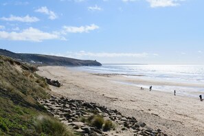 Ein Strand mit felsigem Vordergrund, Sandstrand und blauem Himmel.
