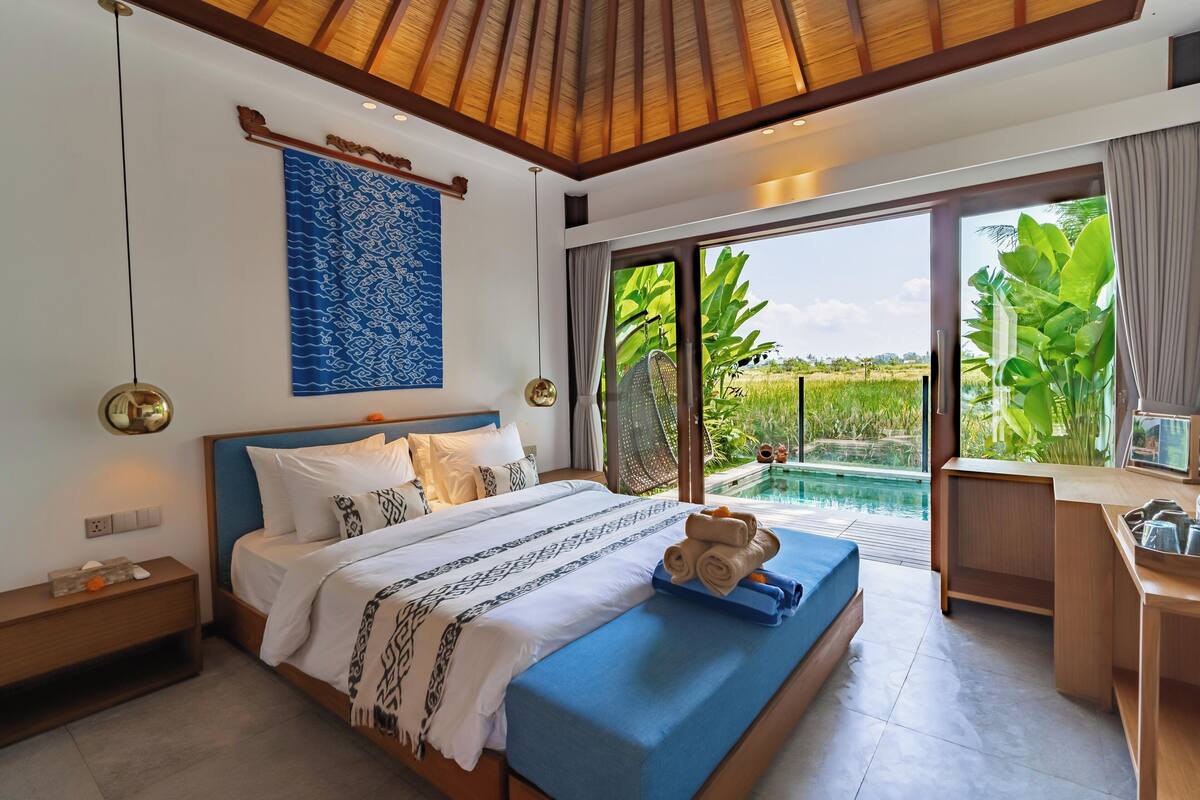 A modern bedroom with a large bed, a desk, and a view of a swimming pool.