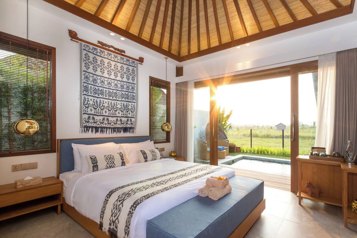 A spacious bedroom with a large bed, a view of a lush green field, and a wooden ceiling.