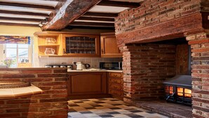 A rustic kitchen with exposed wooden beams, a brick fireplace, and a checkered floor. - Cottage in Derbyshire with Private Garden (Ashbourne)