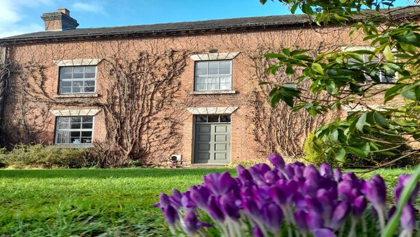 A brick building with three windows and a door, surrounded by greenery and purple flowers. - Cottage in Derbyshire with Private Garden (Ashbourne)