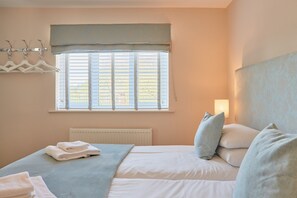 A bedroom with a bed, a radiator, a window with blinds, a wall-mounted light, and a coat rack with hangers. - Countryside retreat with hot tub, No Deposit (Ashbourne)